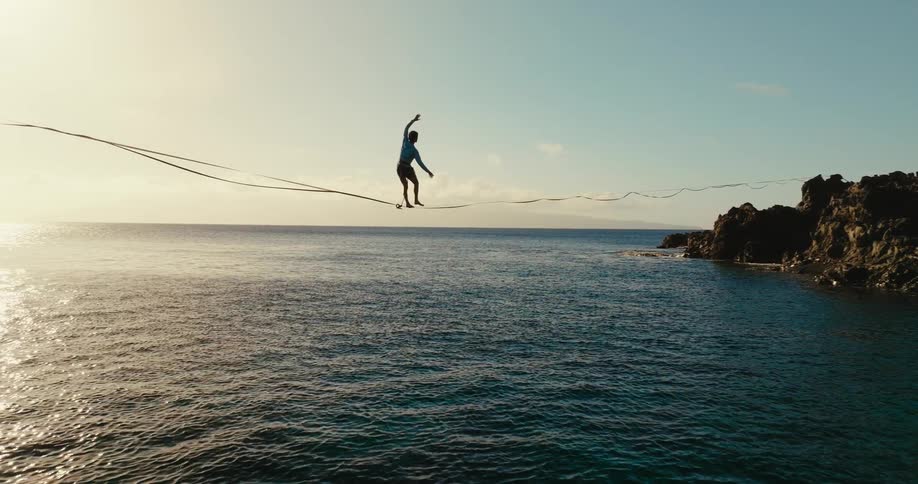 A man balances on a tightrope on the shore