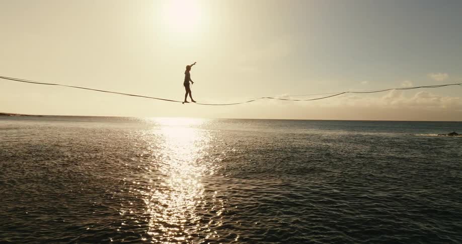 Silhouette of man slacklining over the ocean at sunset