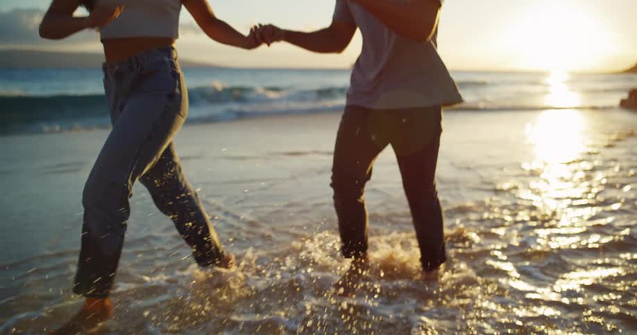 Smiling couple running hand in hand along the shoreline at sunset