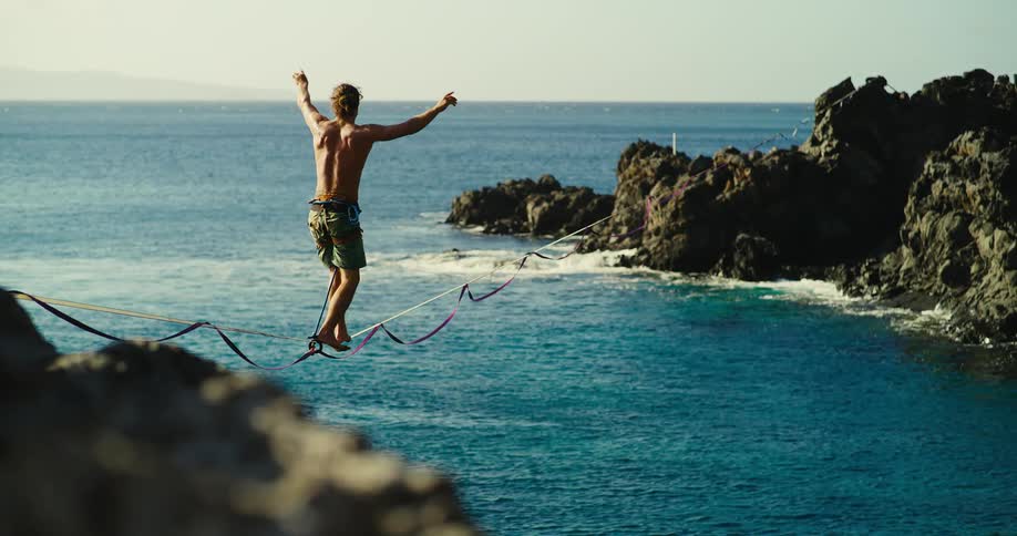 Man practicing slackline over the sea balancing on a rope stretched between rocks