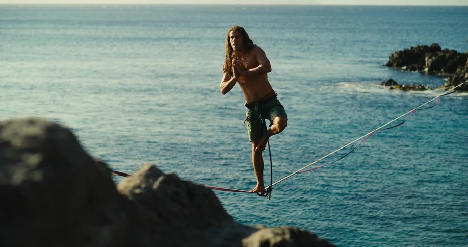 A man balances on a slackline over the ocean in a yoga pose