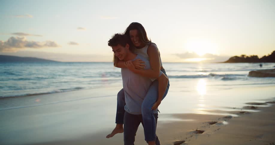 A man gives a woman a piggy back ride on the beach