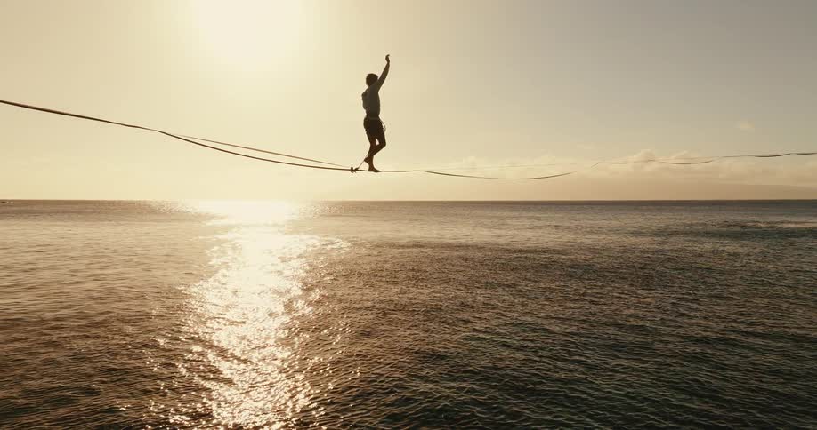 Silhouette of a man walking across a tightrope over the ocean at sunset
