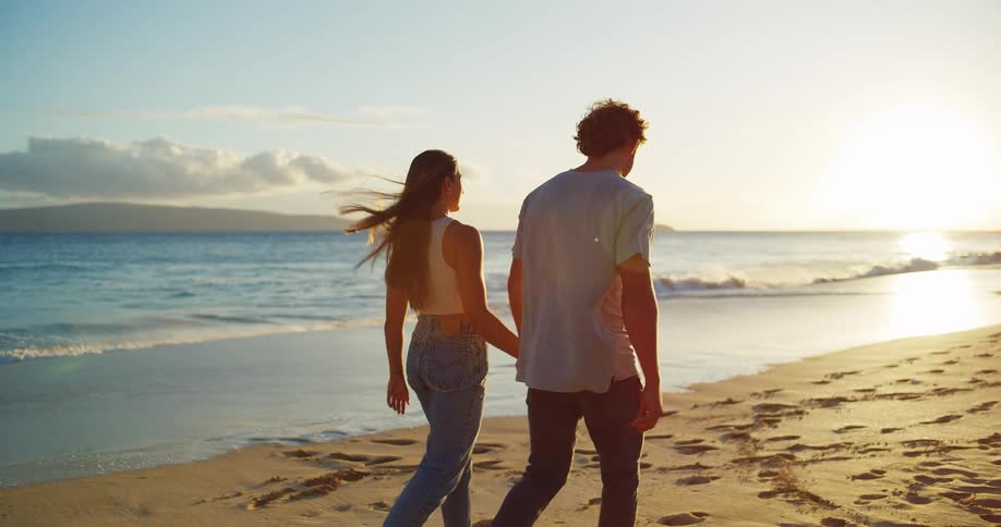 A young fully dressed couple walking along the waters edge on the beach while holding hands