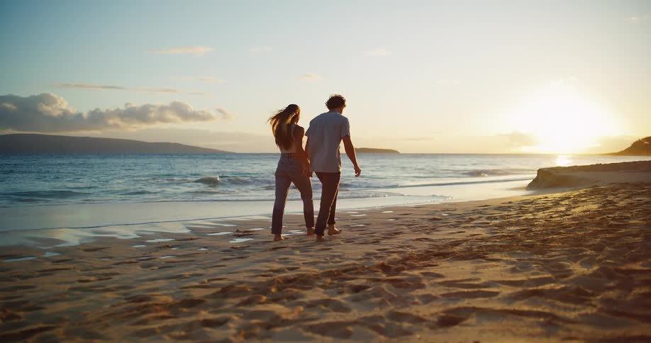 Couple walking hand in hand along the beach at sunset leaving footprints in the sand