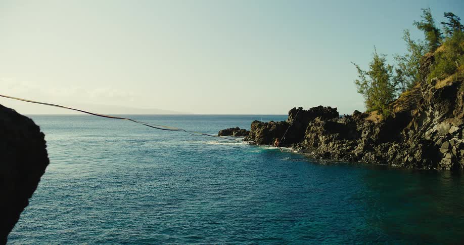A person slacklines over the ocean near rocky cliffs