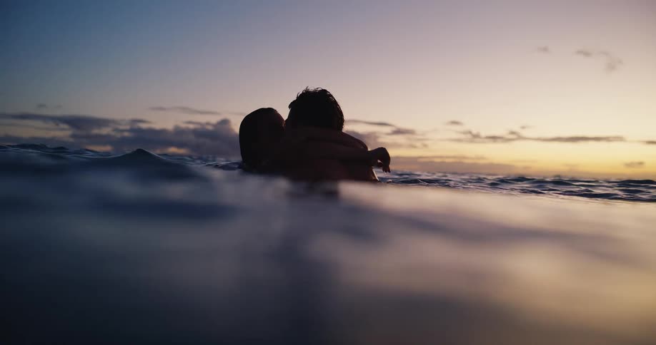 Couple kissing in the sea at sunset partially lit by the colorful sky