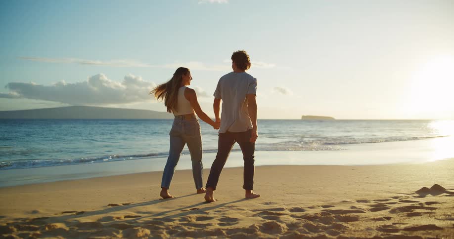 Couple walking hand in hand on the sandy beach at sunset