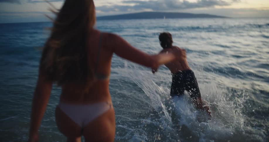 Back of a couple running and diving into the ocean at sunset
