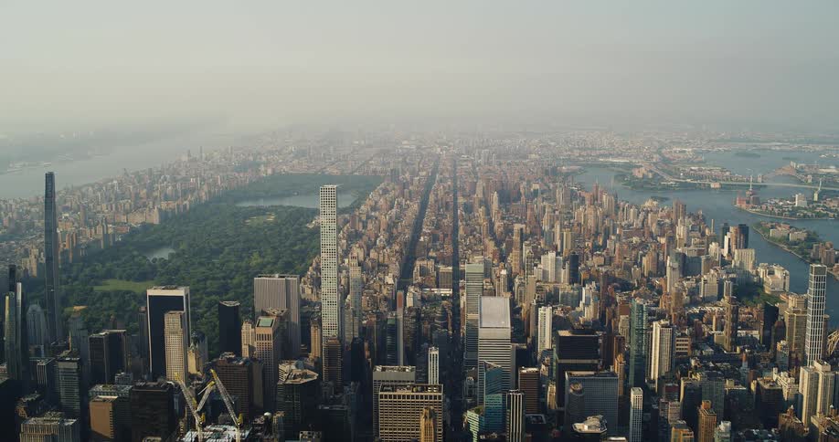 A wide aerial shot of a city on a hazy day with a clear view of a park and a lot of densely packed skyscrapers