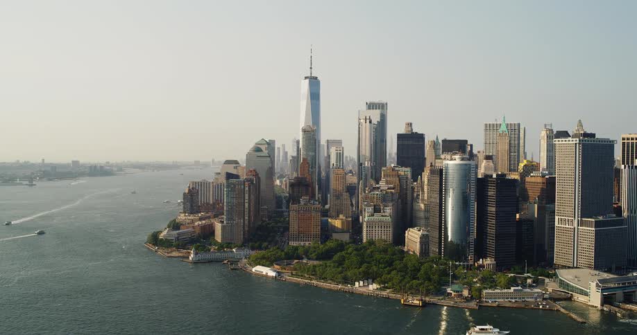 The Freedom Tower in New York City - An aerial view of a city showcasing a dense collection of skyscrapers along the waterfront under a hazy sky with boats moving on the water