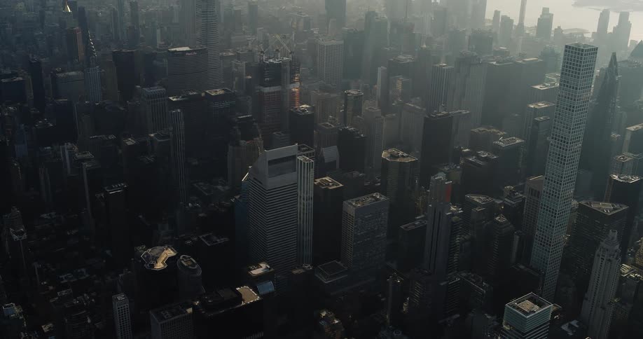 A slowmoving aerial shot captures the vast dense skyline of a major city filled with skyscrapers partially obscured by morning haze and sunlight