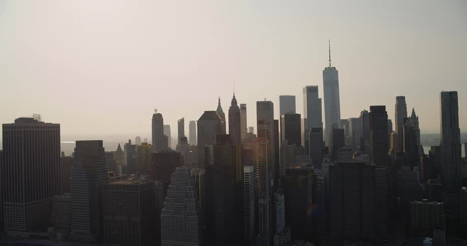 An aerial shot shows a panoramic view of the new york city skyline on a cloudy day the camera slowly zooms in with the empire state building and one world trade center standing tall among the other skyscrapers