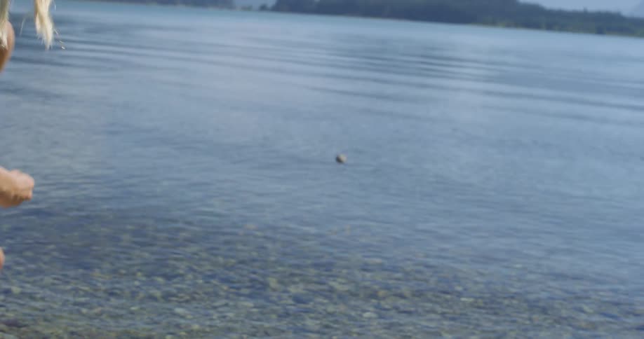 Woman throws a stone into the clear water of a lake