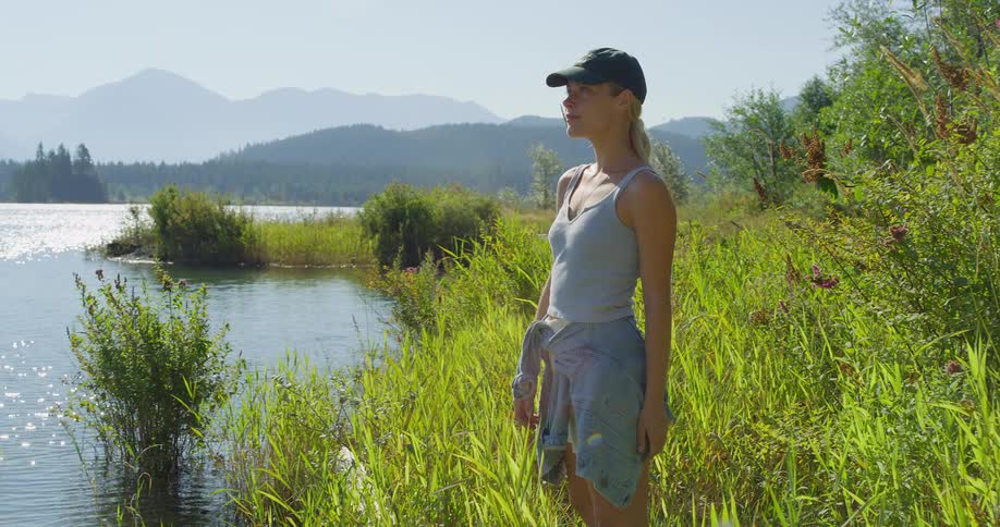 Woman poses by a bright lakeshore with mountains beyond