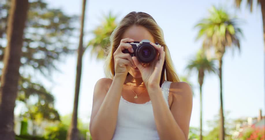 The woman is snapping pictures by the palm trees