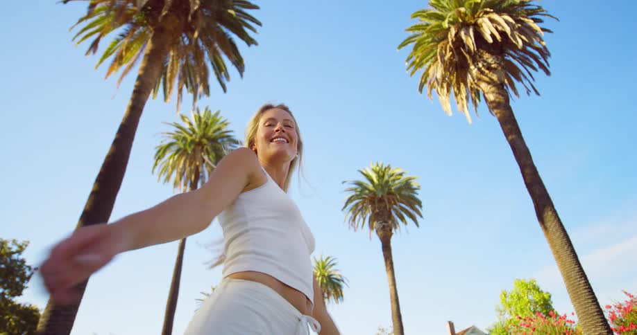 The woman is smiling and spinning by the palm trees