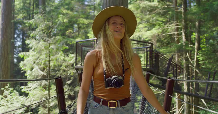 A woman smiles as she walks along a bridge suspended between two trees