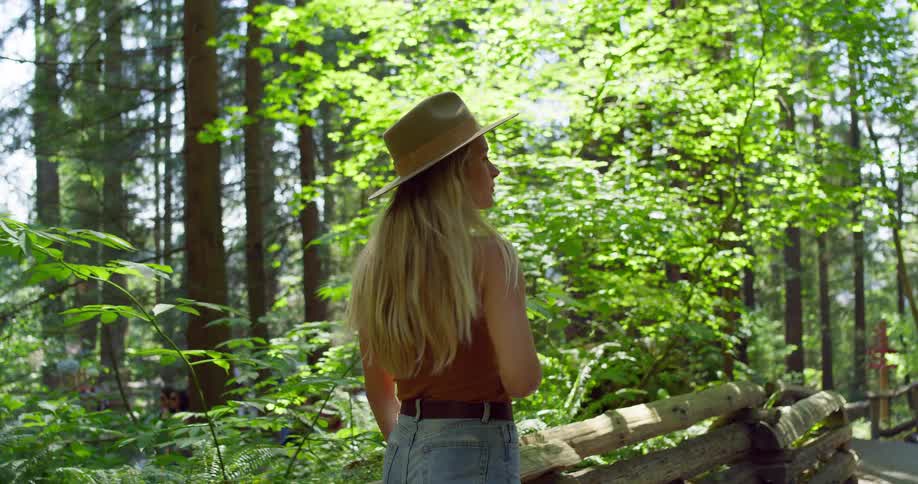 Woman wearing a hat walks smiling along a trail surrounded by trees
