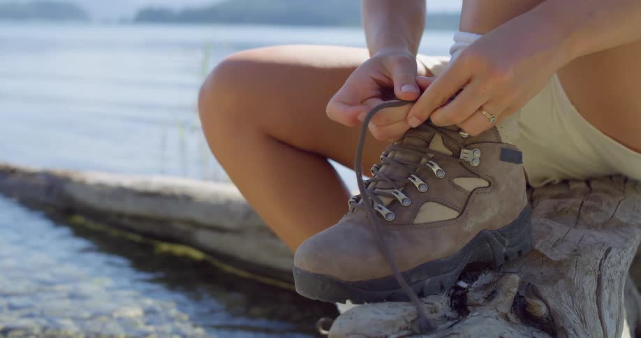 Female sitting on a log next to lake tying laces on her hiking boots