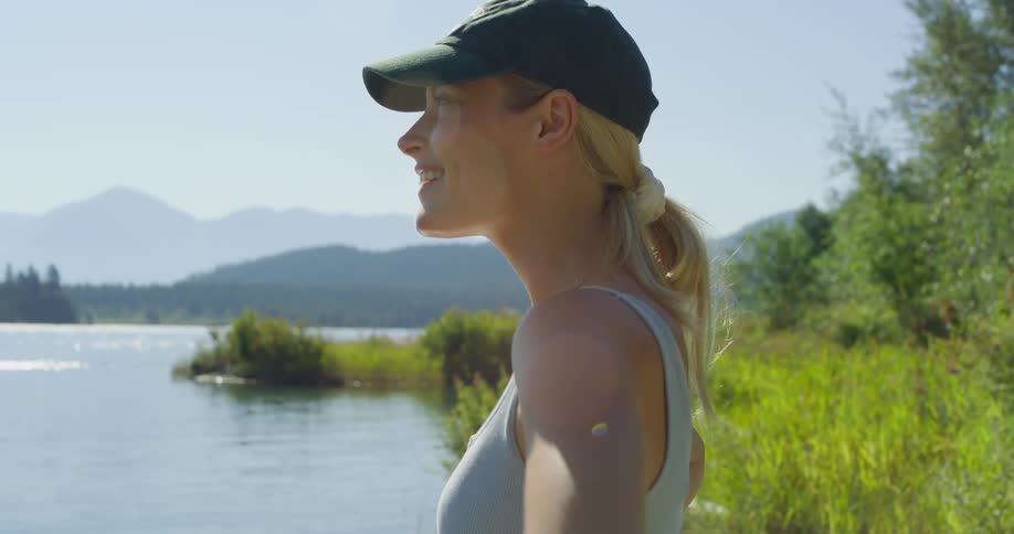 Woman smiles while enjoying the view by a lake surrounded by mountains