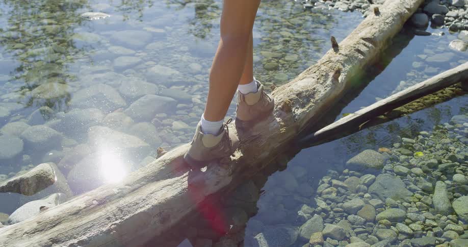 Woman in boots walking on a fallen log in a lake
