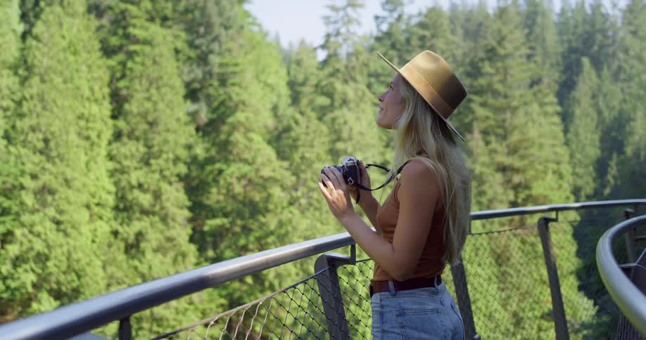 Woman with a hat taking photos on a suspended walkway surrounded by dense forest