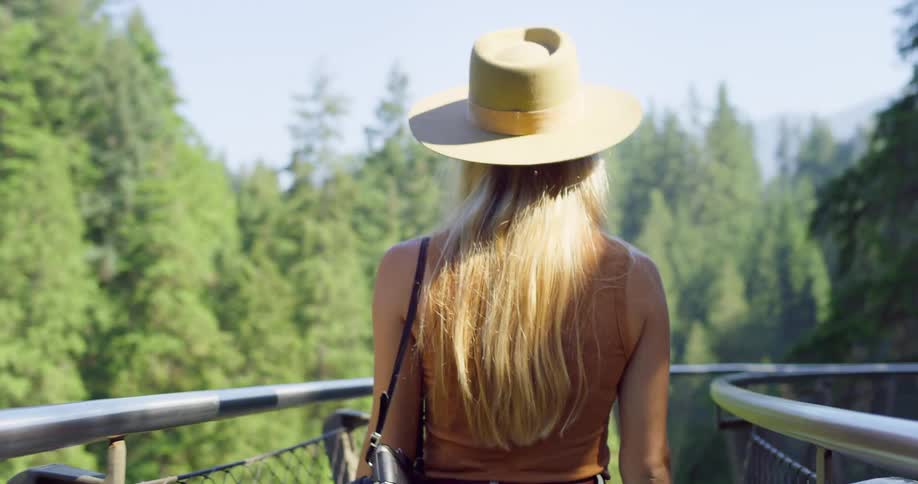 The woman walks on the bridge above the forest