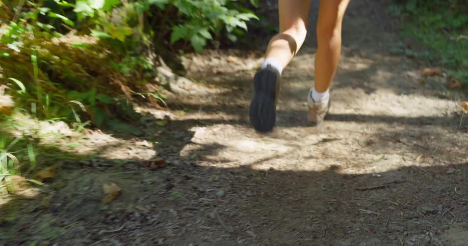 A young woman wearing a hat shorts and sneakers hiking on a path in the woods with a backpack at midday laughing and enjoying herself