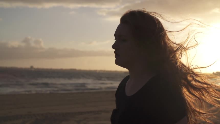 A depressed looking woman walking on beach at sunset