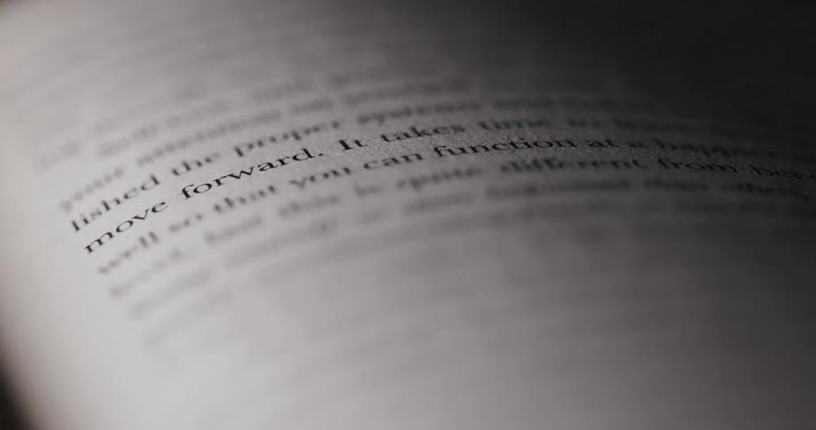 A close view of an open book shows a page with black text as the light casts a harsh shadow from the top right across the rest of the page