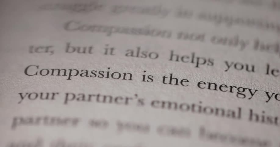 A shot shows the pages of a book with the words compassion is the energy y visible on the page the text is blurry and out of focus with only a few words clearly visible