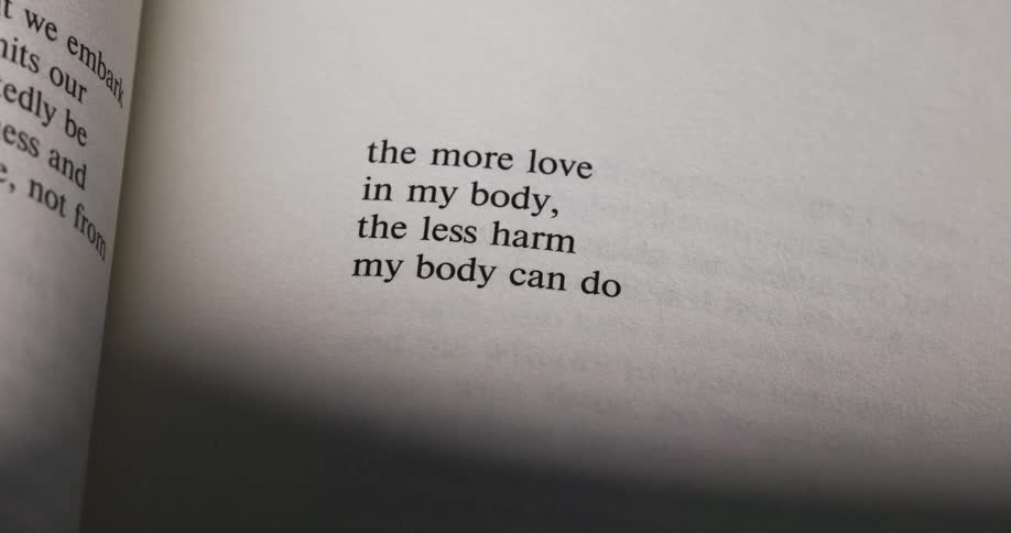 The camera focuses on an open book displaying two lines of text the more love in my body the less harm my body can do the text is a poem written by rupi kaur