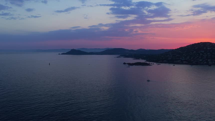 Mountains along the coast and rocks in the water under a colorful sunset sky