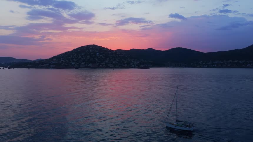 Sailboat sails on calm sea during sunset with mountains in the background