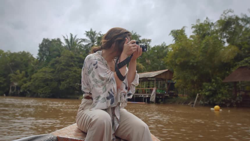 Woman taking a photo while sitting on a boat in a tropical river village