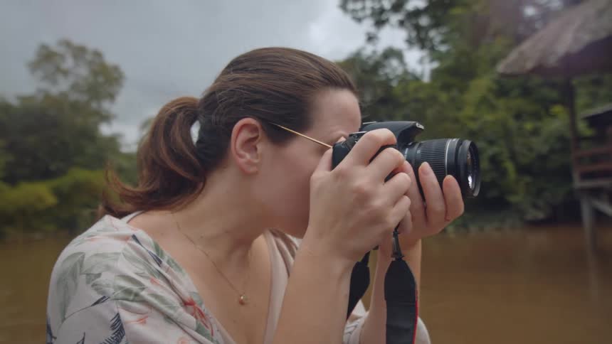 Woman taking photos with a camera near a river in a forest area