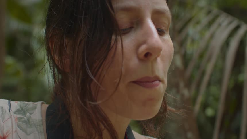 A woman is shown tasting a white fruit from a cocoa pod in a natural leafy environment
