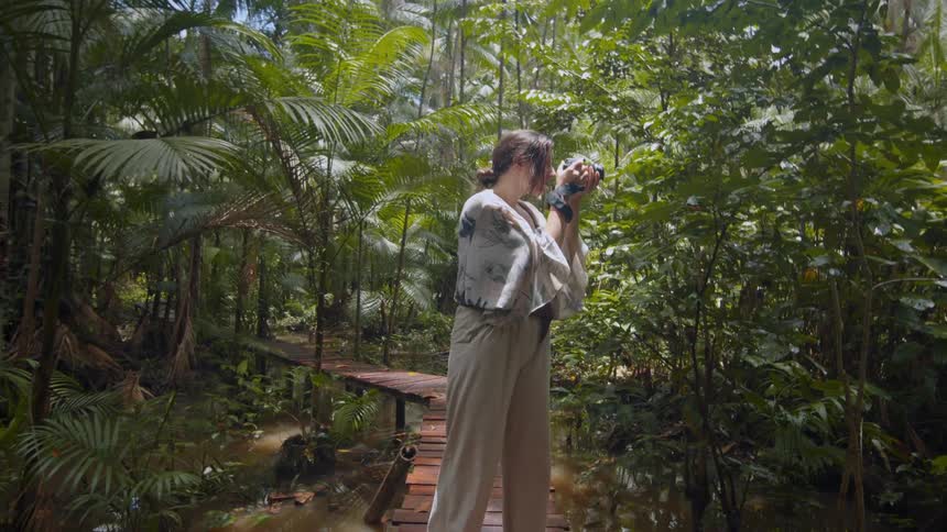 A woman is walking on a wooden bridge in a marsh taking photographs