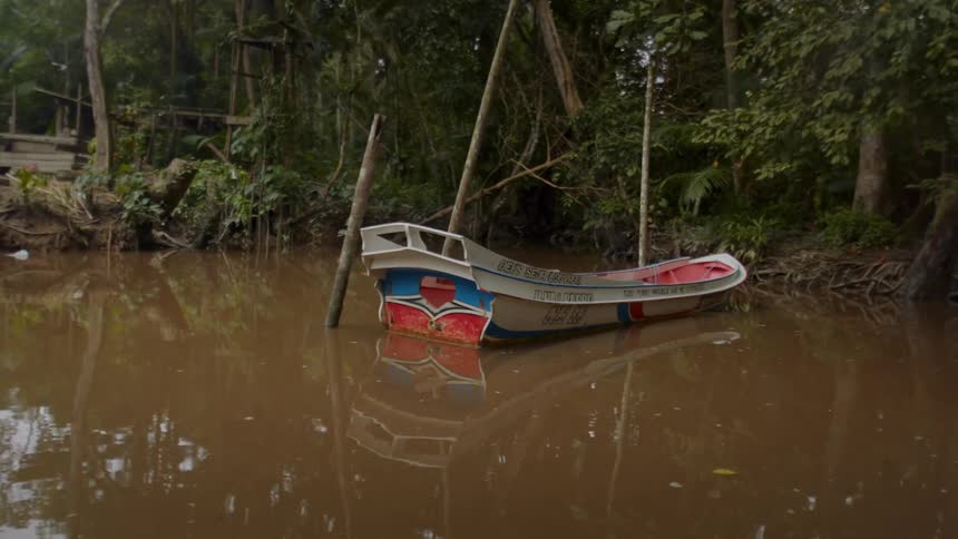 The video shows a small colorful boat moored in murky brown water on the side of the boat there are two lines of text deus seja louvado and tudo posso naquele que me fortalece