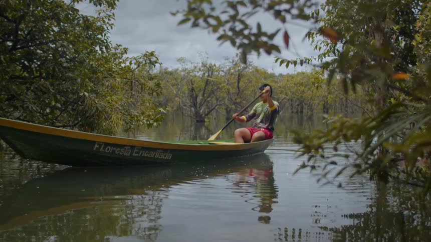 A young man rows a boat on a calm river during daytime