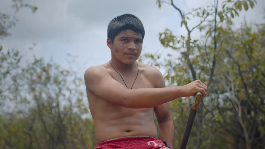 Shirtless man paddling in a flooded forest environment