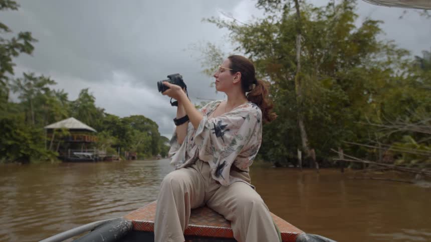 The woman takes a picture and smiles on the rowboat