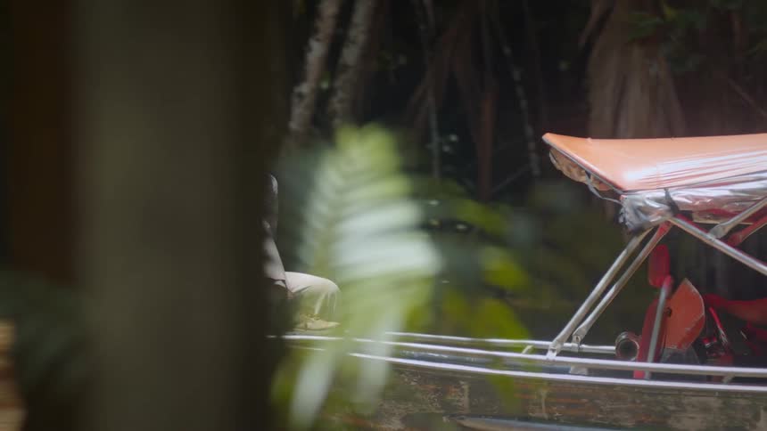 Woman sitting at the bow of a boat with an orange canopy holding a camera while navigating a river surrounded by dense vegetation