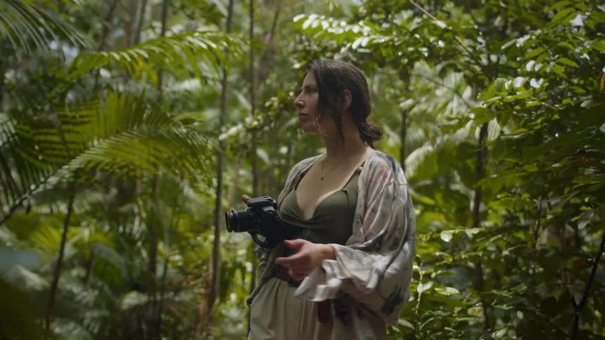 Woman taking photographs amidst the dense vegetation of a tropical forest