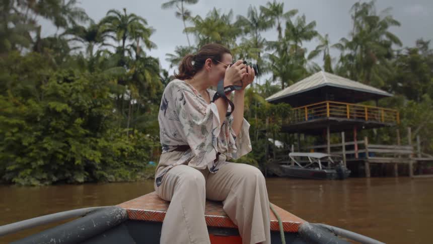 Woman sitting on the bow of a boat photographs the riverside landscape