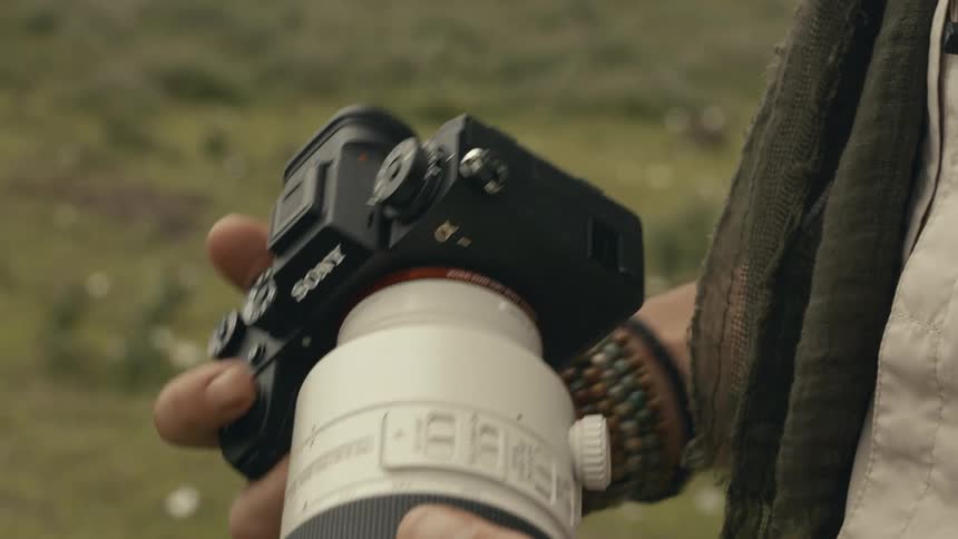 Detail shot of a camera fitted with a white telephoto lens in the field