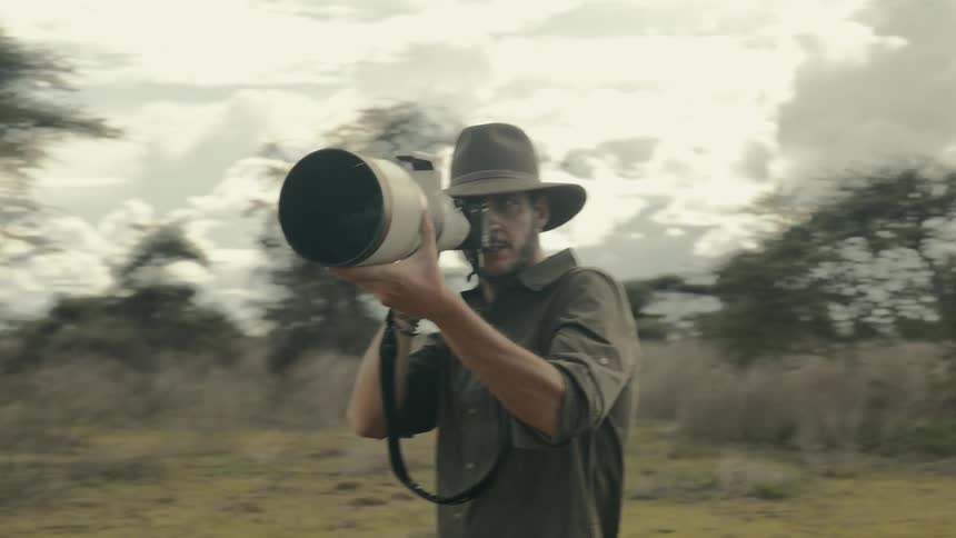 A man with a wide brim hat photographs wildlife on the plains