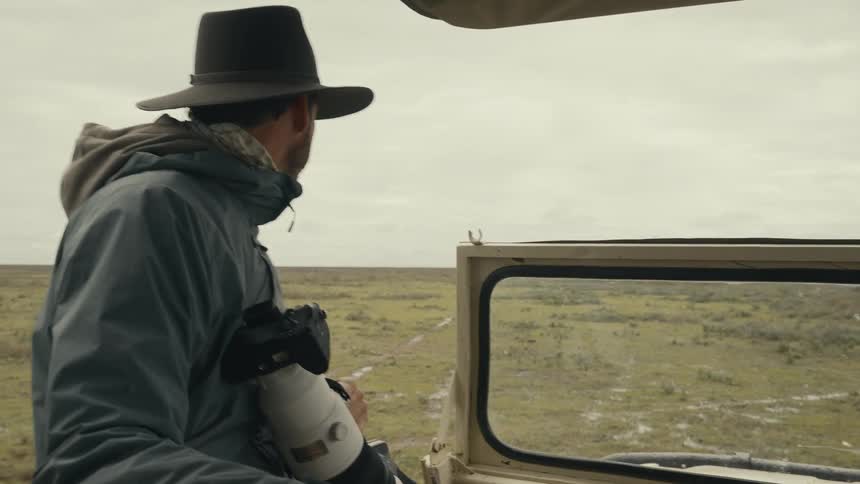 A photographer sits in a car as it moves through a grassland