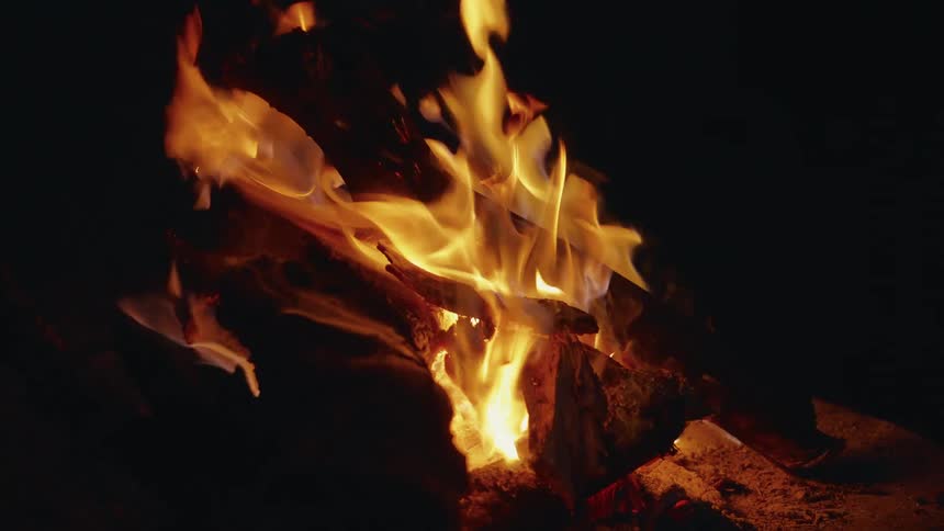 Campfire with bright flames lighting up pieces of wood at night